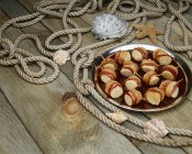 Vue surélevée des pétoncles enveloppés de bacon sur des planches de bois avec corde et coquilles — Photo de stock