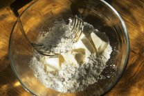 Vista superior de las piezas de mantequilla en la harina con la batidora de pastelería en el tazón de vidrio - foto de stock