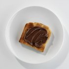 Vista close-up de torrada com manteiga de chocolate na placa branca — Fotografia de Stock