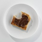Gros plan vue de dessus de pain grillé mordu avec du beurre de chocolat sur plaque blanche — Photo de stock