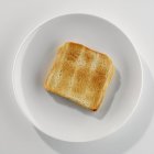 Primer plano vista superior de una rebanada de pan tostado en un plato blanco - foto de stock
