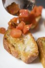Poner tomates en cubitos en rebanada de baguette tostada - foto de stock