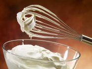 Closeup view of whipping cream in a glass bowl with a whisk — Stock Photo
