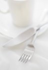 Primo piano vista di forchetta e coltello vicino tazza bianca e piattino — Foto stock