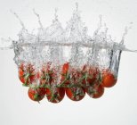 Tomates de vid que caen al agua - foto de stock