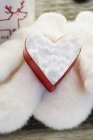 Closeup view of heart-shaped biscuit cutter filled with snow on fur mittens — Stock Photo