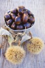 Chestnuts in bowl on wooden table — Stock Photo