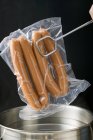 Putting frankfurters in bag into pan — Stock Photo