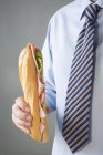 Businessman holding ham sandwich — Stock Photo