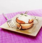 Cipolle avvolte in pancetta su piatto quadrato con forchetta su superficie viola — Foto stock
