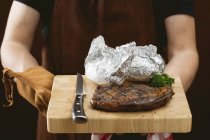 Man holding steak with baked potatoes — Stock Photo