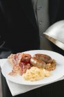 Butler sirve desayuno inglés en el plato con cubierta de cúpula - foto de stock