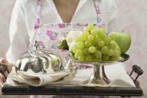 Closeup cropped view of woman in apron holding tray with fresh fruit — Stock Photo