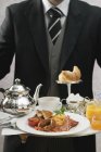 Maggiordomo che serve colazione inglese su vassoio — Foto stock