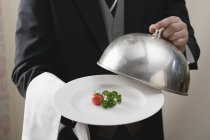Butler servindo tomate e salsa na placa com tampa de cúpula nas mãos, parte central — Fotografia de Stock