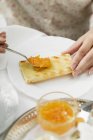 Руки з ложкою Розтягування помаранчевого мармеладу на тості на білій тарілці — стокове фото