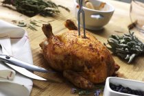Closeup view of roast chicken with fork, scissors and herbs — Stock Photo