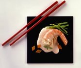 Nahaufnahme von oben: Riesengarnele mit Fischstücken, Kräutern und Sauce auf schwarzem Teller mit roten Essstäbchen — Stockfoto