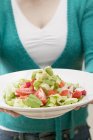 Woman holding plate of salad with avocados and tomatoes in hands, midsection — Stock Photo