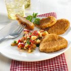 Хлебные куриные эскалопы с овощами на белой тарелке с вилкой — стоковое фото