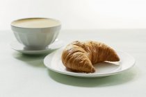 Café leitoso com croissant na placa — Fotografia de Stock