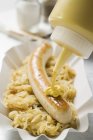 Putting mustard on sausage with sauerkraut — Stock Photo