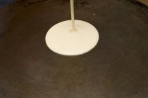 Nahaufnahme des Gießens rohe Crêpe-Mischung auf heißer Platte — Stockfoto