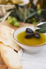 Olivenöl in Schüssel mit schwarzen Oliven — Stockfoto