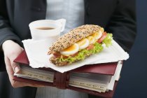 Closeup view of woman holding sandwich and drink on organiser — Stock Photo