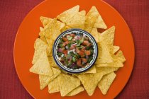 Tomato salsa with tortilla chips on orange plate with bowl — Stock Photo
