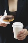 Woman holding doughnut and coffee cup — Stock Photo