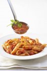 Penne pasta on plate and ladle with sauce — Stock Photo