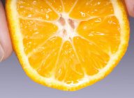 Mano apretando mandarina mitad naranja - foto de stock