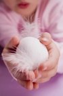 Обрезанный вид ребенка, держащего белое яйцо с перьями — стоковое фото