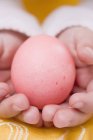 Крупный план детских рук, держащих красное яйцо — стоковое фото