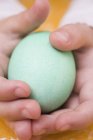 Vista close-up de mãos de criança segurando um ovo verde — Fotografia de Stock