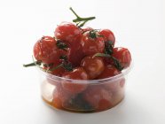 Tomates cereja assados em recipiente de plástico sobre fundo branco — Fotografia de Stock