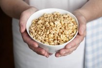 Cropped view of hands holding a bowl of puffed wheat cereal — Stock Photo