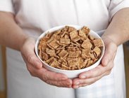 Vista de cerca de las manos sosteniendo un tazón de cereal de desayuno con sabor a canela - foto de stock