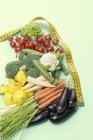 Assorted baby vegetables with tape measure on green surface — Stock Photo