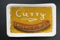 Top view of a Currywurst sausage in curry powder on a paper plate — Stock Photo