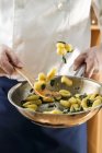 Обрезанный вид повара, бросающего шалфей Ньокки в сковородку — стоковое фото
