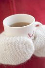 Vista de perto de mãos em mitenes segurando xícara de chá quente — Fotografia de Stock