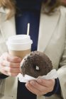 Mulher segurando donut e xícara de café — Fotografia de Stock
