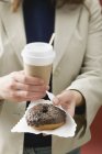 Femme tenant beignet et tasse de café — Photo de stock