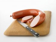 Anneau tranché saucisse de Bologne avec couteau sur planche de bois — Photo de stock