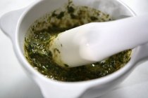 Closeup view of basil Pesto with a pestle in a mortar — Stock Photo