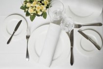 Place setting in white with fabric napkin, wine glasses and flowers — Stock Photo