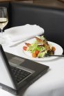 Closeup view of salad with bacon in front of laptop — Stock Photo