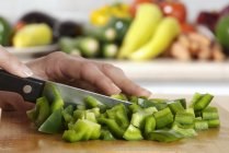Chopping a green pepper on wooden chopping board — Stock Photo